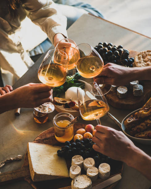 Hands of people clinking glasses with orange or rose wine over snacks cheese grape bread on concrete background. Gathering, celebrating, wine tasting concept